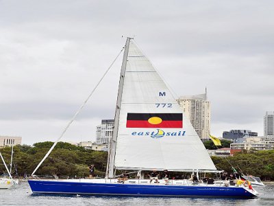 Le "Tribal Warrior" dans le port de Sydney en Australie le 13 décembre, arborant le drapeau aborigène, lors d'un entraînement en amont de la course Sydney-Hobart qui partira ce jeudi. - Saeed KHAN [AFP]